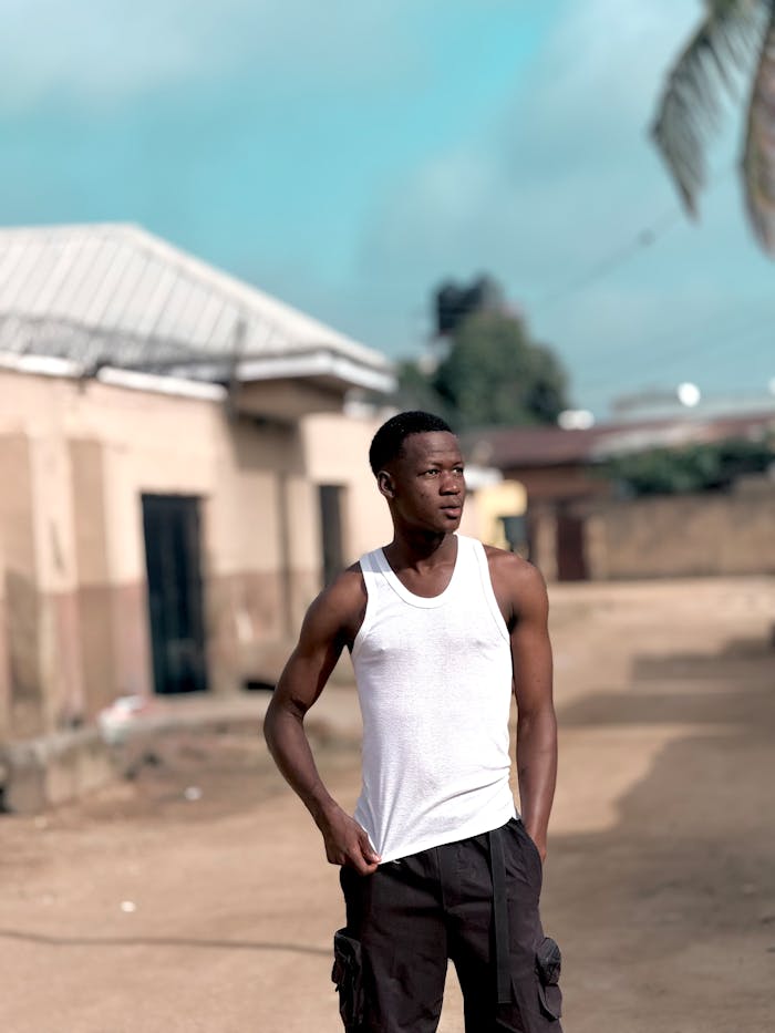 Casually dressed young man stands in a sunny neighborhood street.